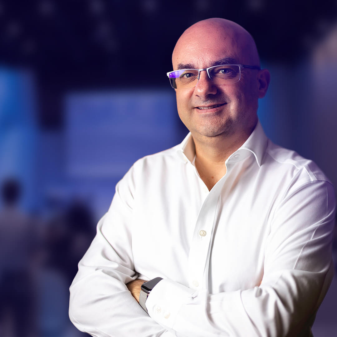 Portrait de Bernard Coulaty, intervenant en keynote lors d’une conférence sur les ressources humaines, en chemise blanche sur fond flou de salle de conférence.