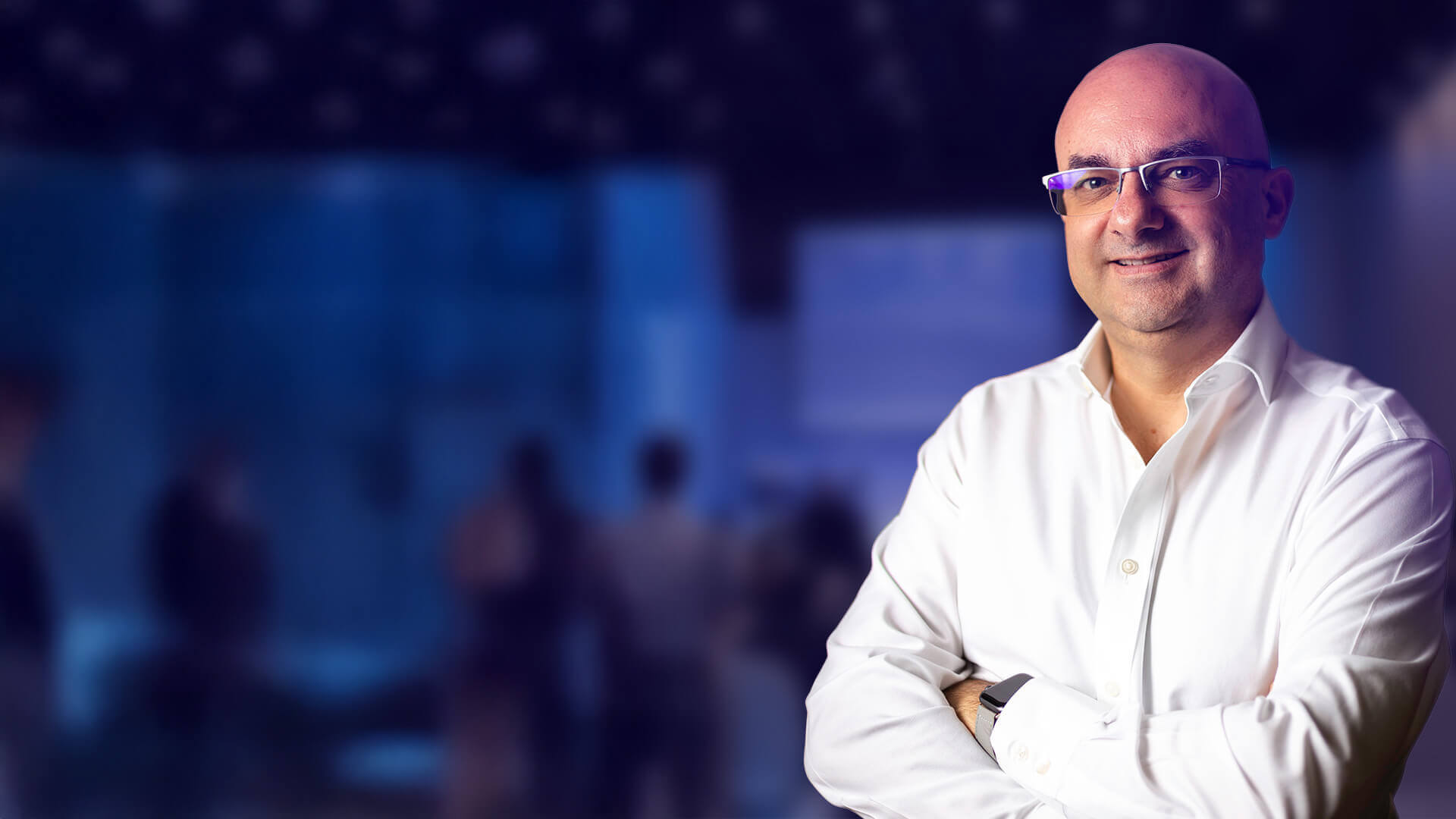 Portrait de Bernard Coulaty, intervenant en keynote lors d’une conférence sur les ressources humaines, en chemise blanche sur fond flou de salle de conférence.